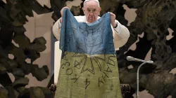 Pope Francis holds up a flag which he said was brought to him from “the martyred city” of Bucha, Ukraine at his general audience on April 6, 2022. Vatican Media