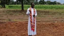 Fr. Sam Ebute prays over a mass grave in Nigeria. / Aid to the Church in Need (ACN)