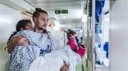 Erik Dike, a rising senior nursing student at Belmont Abbey College, carries a patient onboard a hospital ship in Madagascar during a two-week program with Mercy Ships. / Credit: Joshua Kiew Wing Chau
