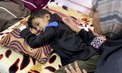 Eight-year-old Yamen Abu Hilal lies on a bed as a woman sits beside him in a hospital room in Gaza City, Gaza Strip, on Nov. 24, 2025.  His condition has sharply worsened amid the collapse of Gaza’s health care system, which has been unable to provide diagnostic tools, medication, or equipment since no medical supplies have entered the Strip following the ceasefire. / Credit: Doaa Albaz/Middle East Images/AFP via Getty Images