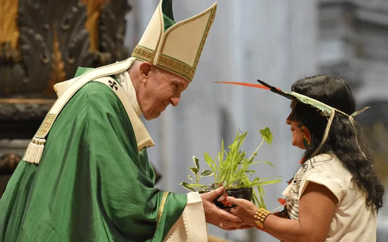 An indigenous woman from the Amazon region hands Pope Francis a plant during the closing Mass of the Synod / Vatican Media