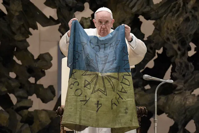 Pope Francis holds a flag that he received from Bucha, Ukraine at his general audience on April 6, 2022. | Vatican Media