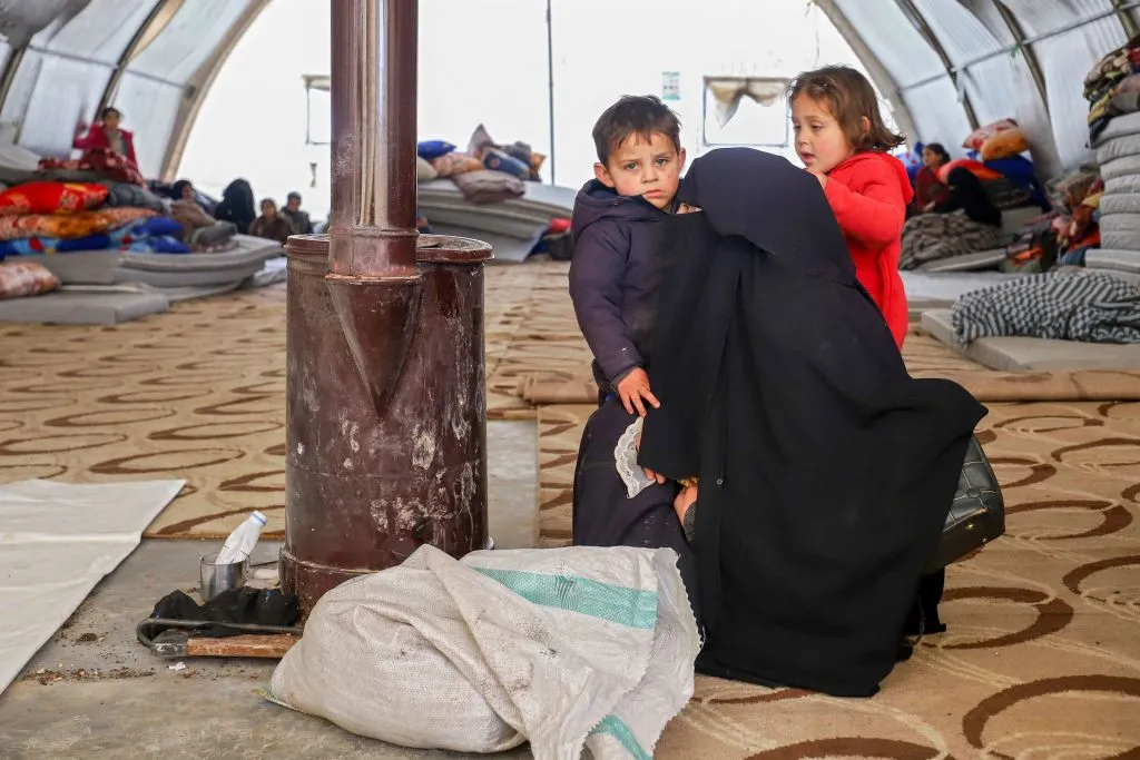 A Syrian woman and her children warm by a stove at an emergency shelter in the center of the city of Maarat Misrin, in the rebel-held northern part of the northwestern Idlib province Feb. 7, 2023, one day after a deadly earthquake hit Syria and Turkey. / Photo by ABDULAZIZ KETAZ/AFP via Getty Images