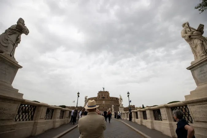 Pilgrims and tourists traverse the historic Ponte Sant'Angelo, flanked by angel sculptures, with Castel Sant'Angelo visible in the distance