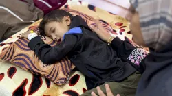Eight-year-old Yamen Abu Hilal lies on a bed as a woman sits beside him in a hospital room in Gaza City, Gaza Strip, on Nov. 24, 2025.  His condition has sharply worsened amid the collapse of Gaza’s health care system, which has been unable to provide diagnostic tools, medication, or equipment since no medical supplies have entered the Strip following the ceasefire. / Credit: Doaa Albaz/Middle East Images/AFP via Getty Images