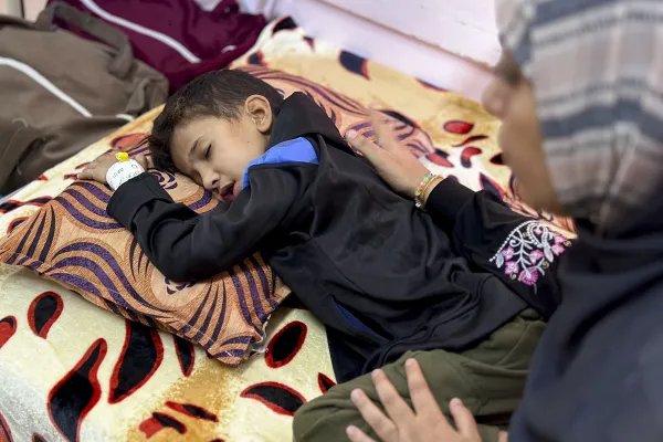 Eight-year-old Yamen Abu Hilal lies on a bed as a woman sits beside him in a hospital room in Gaza City, Gaza Strip, on Nov. 24, 2025.  His condition has sharply worsened amid the collapse of Gaza’s health care system, which has been unable to provide diagnostic tools, medication, or equipment since no medical supplies have entered the Strip following the ceasefire. / Credit: Doaa Albaz/Middle East Images/AFP via Getty Images